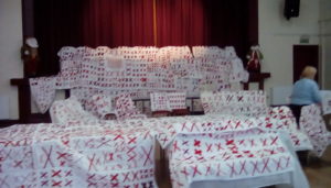 White quilts covered with pairs of red X’s draped over church pews and chairs