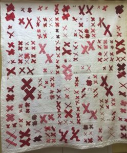 a quilt with a white background covered with pairs of red X's