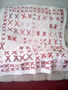 a large white quilt covered with pairs of red X's covers a sofa