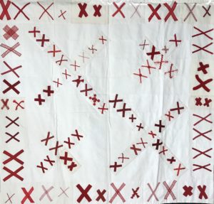white quilt base covered in pairs of red X's, some forming larger red X's