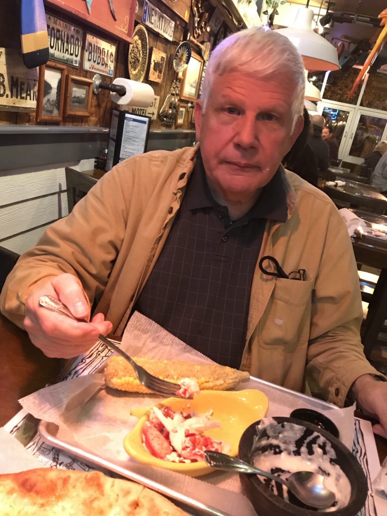 a happy man enjoying fresh lobster and corn on the cob and clam chowder